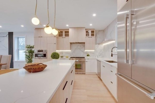 kitchen featuring high end appliances, modern cabinets, custom range hood, pendant lighting, and a sink