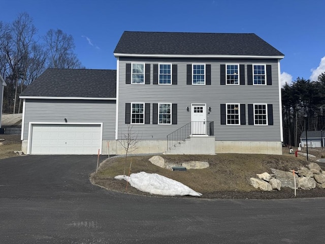 colonial home featuring aphalt driveway, an attached garage, and a shingled roof