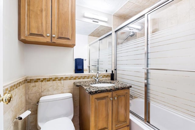 bathroom with wainscoting, toilet, enclosed tub / shower combo, vanity, and tile walls