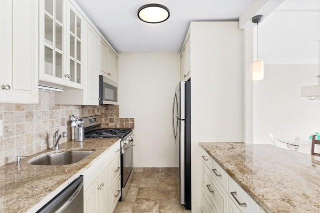 kitchen featuring tasteful backsplash, appliances with stainless steel finishes, glass insert cabinets, a sink, and light stone countertops