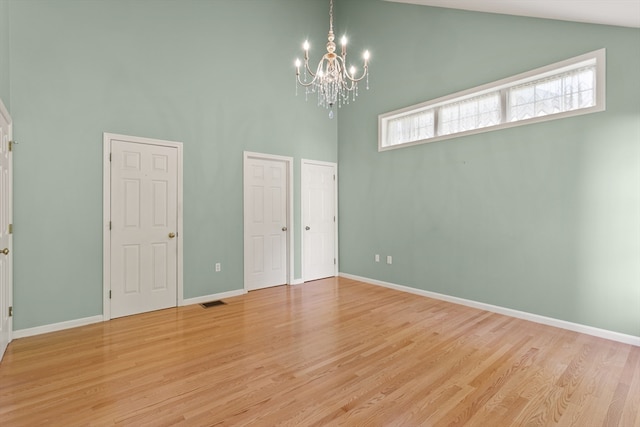 empty room featuring light wood-type flooring, a chandelier, and high vaulted ceiling