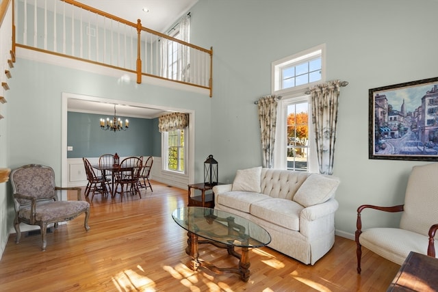 living room featuring ornamental molding, a towering ceiling, light hardwood / wood-style floors, and a chandelier