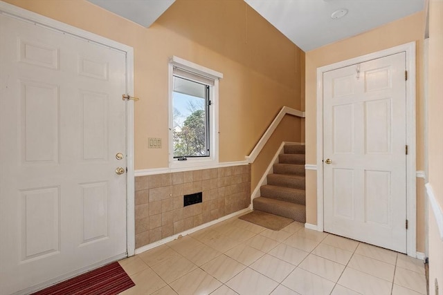 foyer featuring tile walls, wainscoting, stairway, and light tile patterned floors