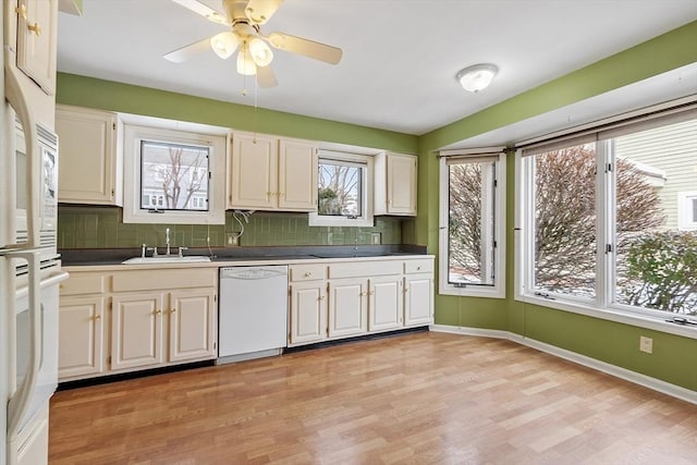 kitchen featuring white dishwasher, a sink, light wood-style floors, baseboards, and backsplash