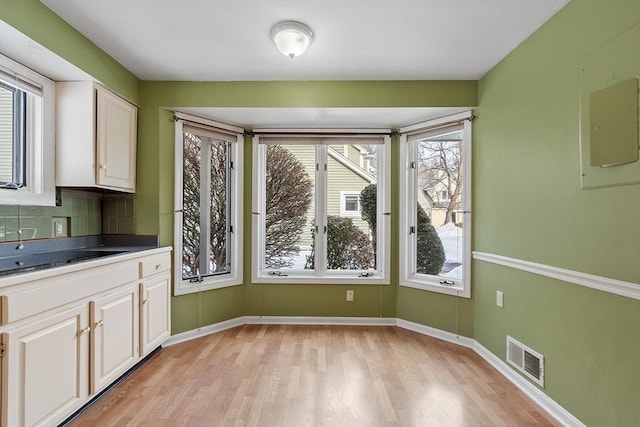 unfurnished dining area with light wood-style flooring, visible vents, and baseboards