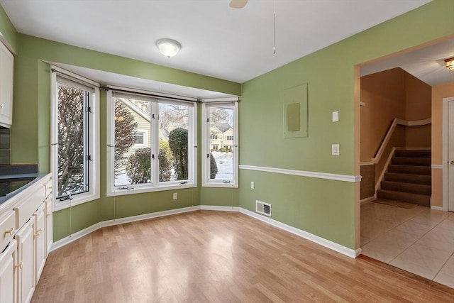 unfurnished dining area featuring light wood-style floors, baseboards, stairs, and visible vents