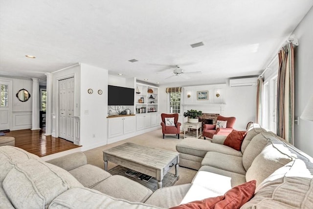 living area with decorative columns, a ceiling fan, a wall mounted AC, and a healthy amount of sunlight