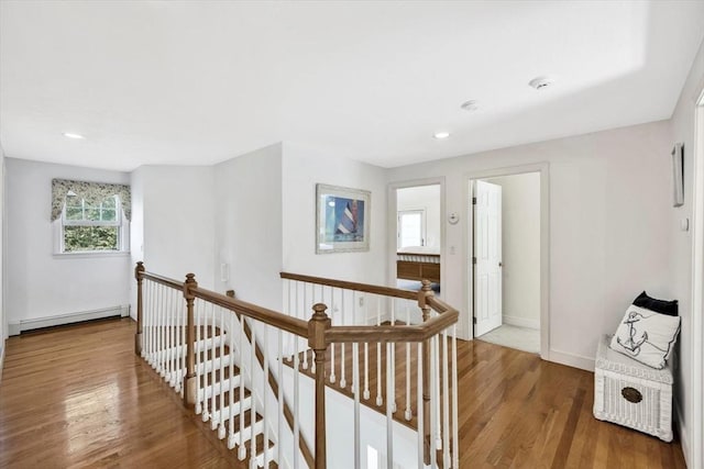 hallway with an upstairs landing, baseboard heating, baseboards, recessed lighting, and wood finished floors