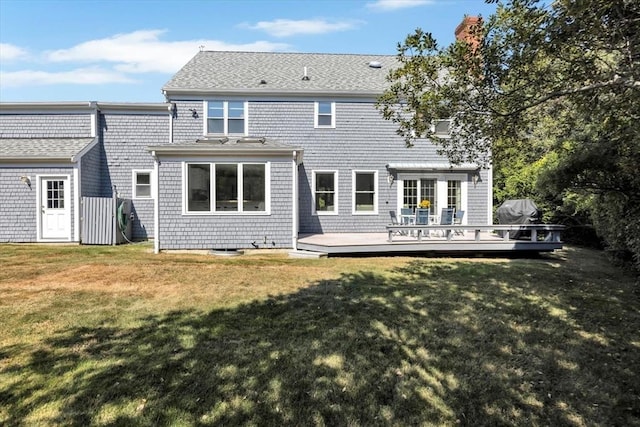 rear view of house featuring a chimney, a shingled roof, a deck, and a lawn