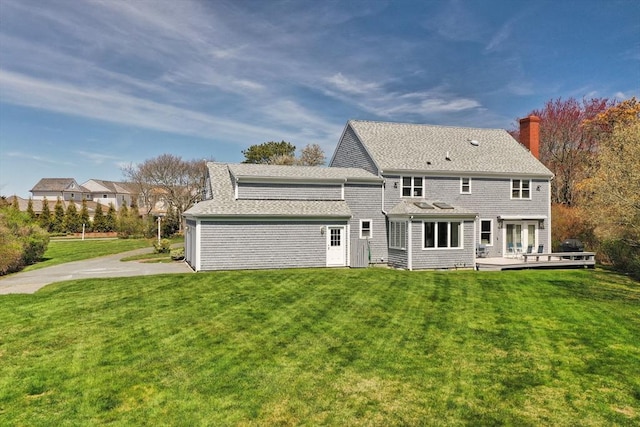 rear view of property with a deck, a chimney, a shingled roof, french doors, and a lawn