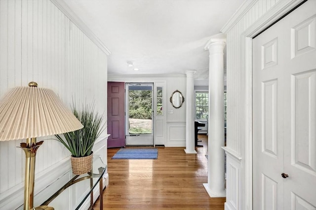 foyer entrance with a decorative wall, light wood-type flooring, ornamental molding, and decorative columns