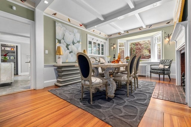 dining space featuring radiator, beam ceiling, wood finished floors, and baseboards