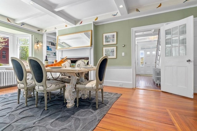 dining area featuring beamed ceiling, radiator heating unit, a wainscoted wall, and wood finished floors