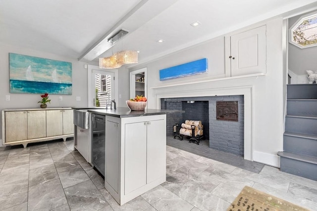 kitchen with marble finish floor, decorative light fixtures, a kitchen island with sink, a fireplace, and dark countertops