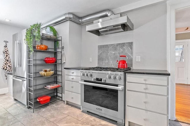 kitchen featuring tasteful backsplash, wall chimney range hood, dark countertops, stainless steel appliances, and white cabinets