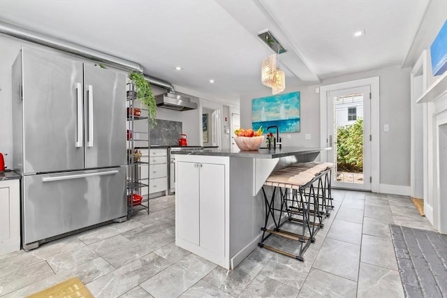 kitchen featuring a sink, a breakfast bar, dark countertops, stainless steel refrigerator, and recessed lighting