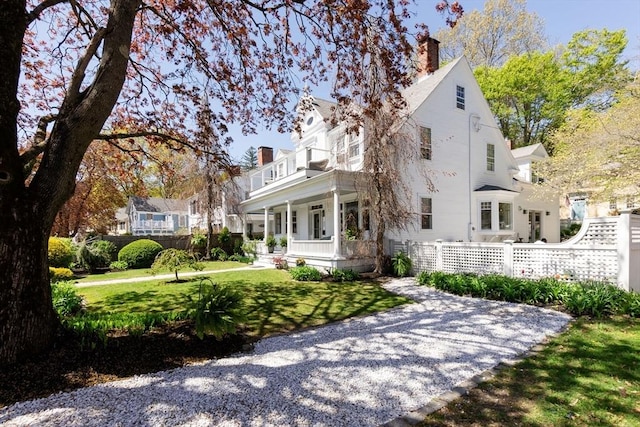 view of front facade with a chimney, a balcony, fence, covered porch, and a front lawn