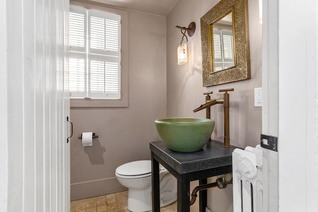 half bathroom featuring radiator heating unit, toilet, baseboards, and a sink