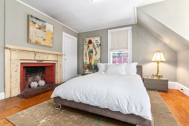bedroom featuring crown molding, a fireplace with flush hearth, and hardwood / wood-style flooring