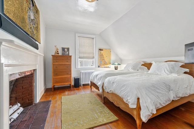 bedroom featuring radiator, lofted ceiling, a fireplace with flush hearth, and hardwood / wood-style flooring