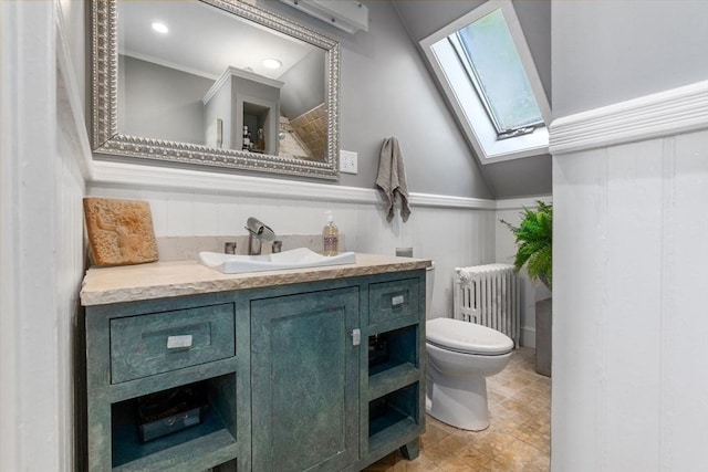 bathroom with toilet, radiator heating unit, wainscoting, vanity, and a skylight