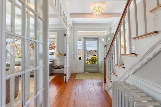 entrance foyer featuring stairs, radiator, hardwood / wood-style floors, beam ceiling, and a notable chandelier