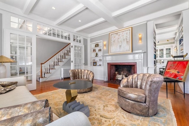 living area featuring built in features, beam ceiling, a fireplace with flush hearth, and wood finished floors