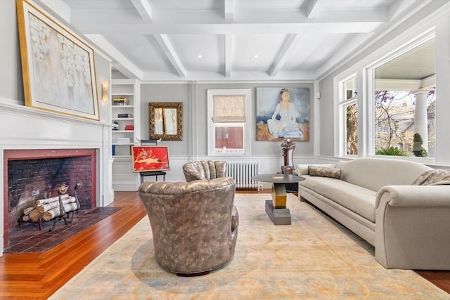 sitting room with radiator, built in features, a fireplace with flush hearth, wood finished floors, and beamed ceiling