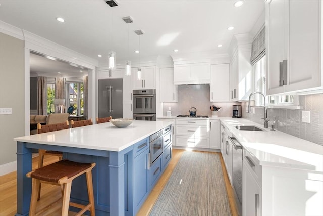 kitchen with a breakfast bar, blue cabinetry, appliances with stainless steel finishes, white cabinets, and a sink