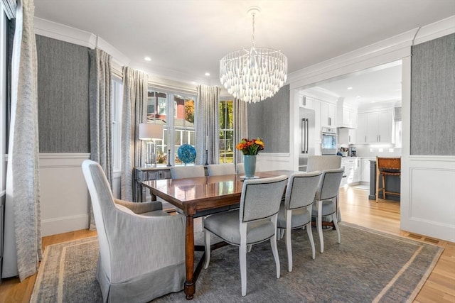 dining space with recessed lighting, a wainscoted wall, a notable chandelier, light wood-style floors, and crown molding