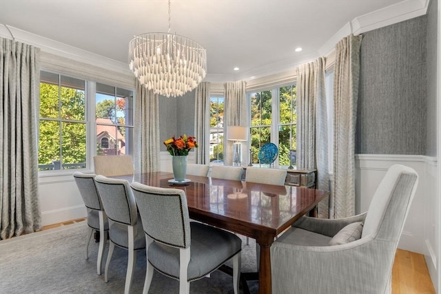 dining space featuring a wainscoted wall, crown molding, a notable chandelier, a decorative wall, and light wood-type flooring