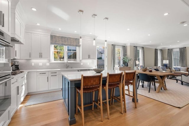 kitchen featuring light wood finished floors, open floor plan, a center island, light countertops, and white cabinetry