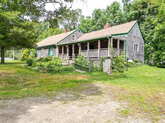 view of front of house with covered porch, a front lawn, a chimney, and a shingled roof