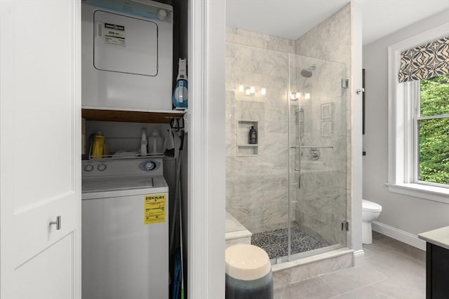 bathroom with stacked washer / dryer, a shower stall, toilet, baseboards, and vanity