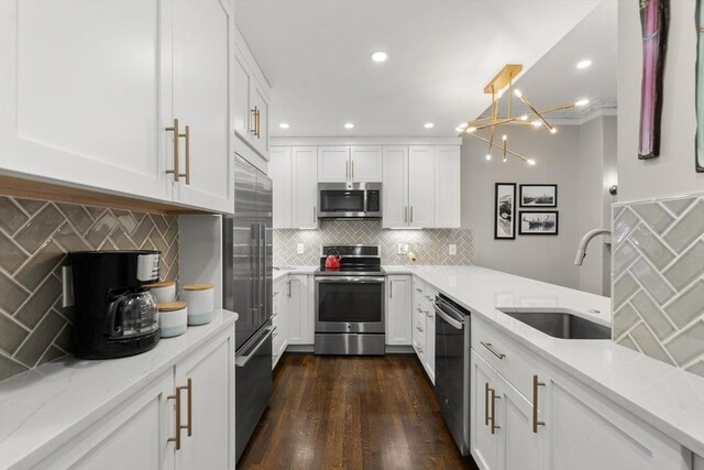 kitchen featuring appliances with stainless steel finishes, a sink, backsplash, white cabinetry, and light stone counters