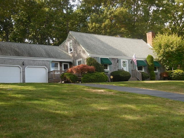 new england style home featuring driveway, a shingled roof, and a front yard