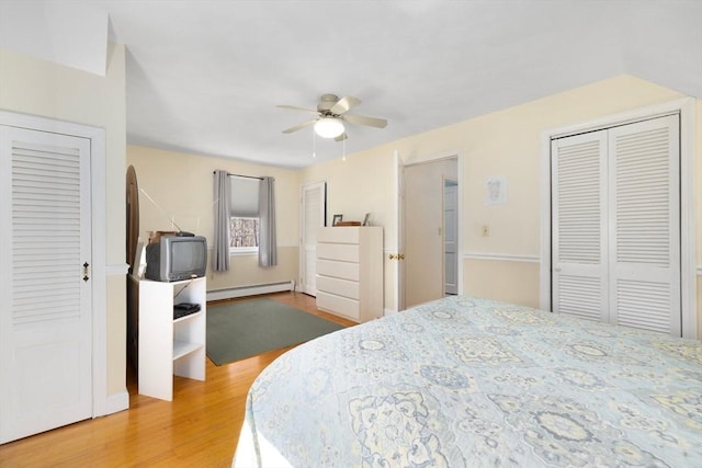 bedroom with ceiling fan, a baseboard radiator, two closets, and wood finished floors