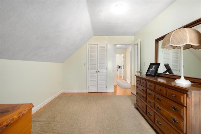 bedroom featuring light wood-type flooring, lofted ceiling, a textured ceiling, a closet, and baseboards