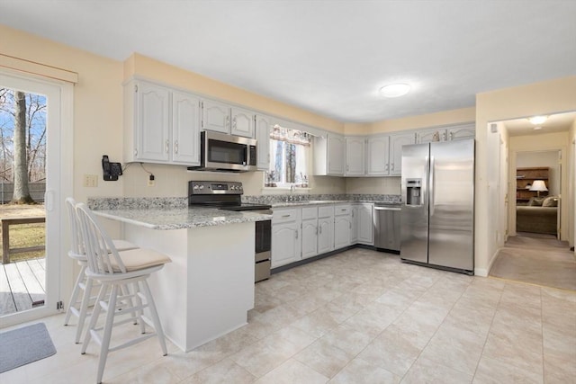 kitchen with light stone counters, stainless steel appliances, a peninsula, a breakfast bar area, and baseboards