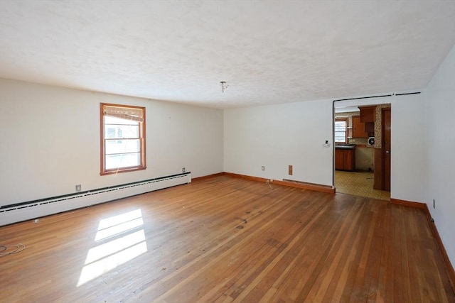 unfurnished room with a baseboard heating unit, a textured ceiling, a healthy amount of sunlight, and wood-type flooring