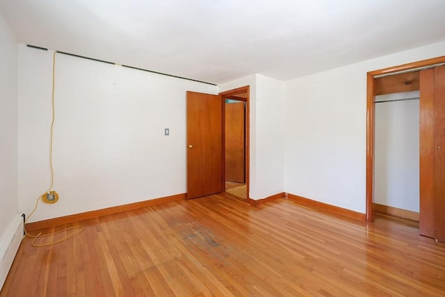 unfurnished bedroom with light hardwood / wood-style floors, a closet, and a baseboard heating unit