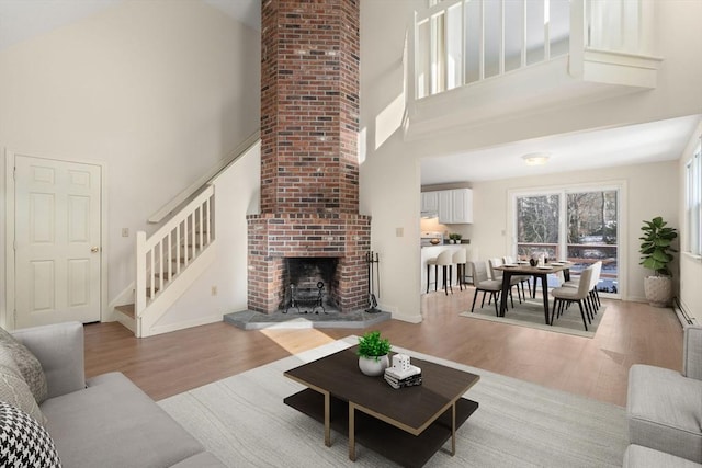 living room featuring a high ceiling, a brick fireplace, and light wood-type flooring