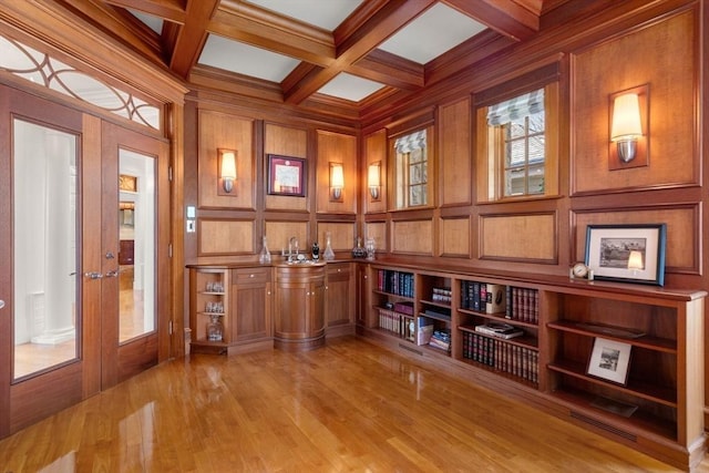 interior space featuring light wood-style flooring, french doors, beam ceiling, coffered ceiling, and a decorative wall