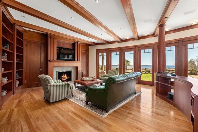 living room featuring a warm lit fireplace, beamed ceiling, and plenty of natural light