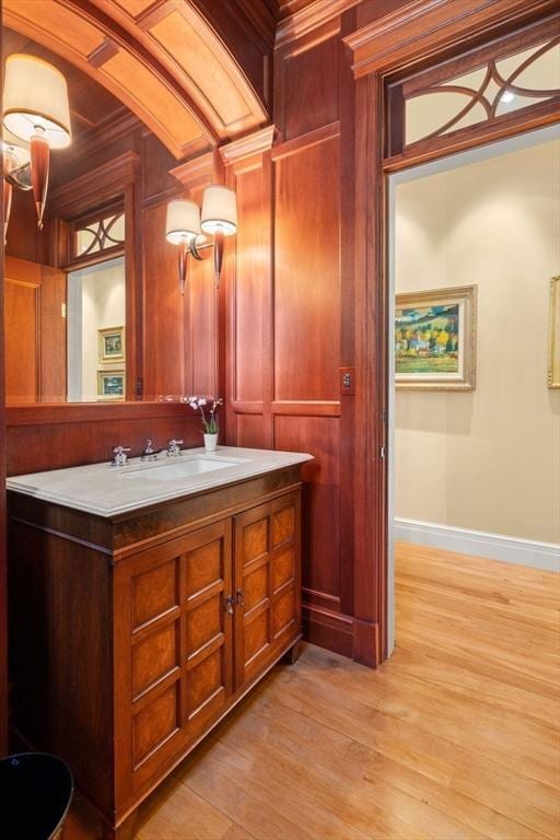 bathroom featuring wood finished floors, vanity, wood walls, and baseboards