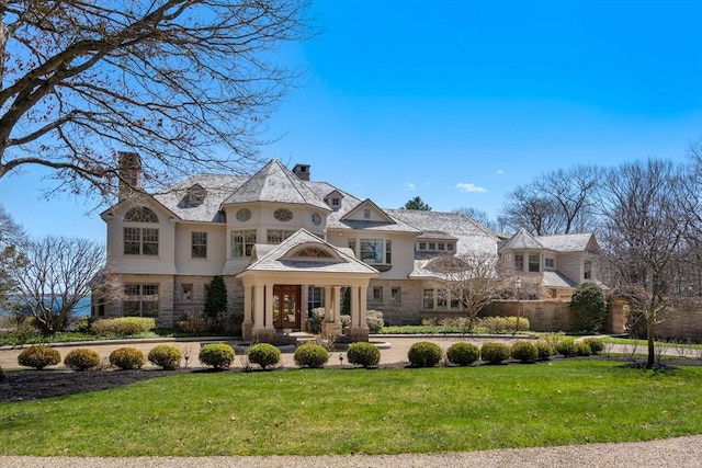 view of front of house with stone siding, a front yard, and a chimney
