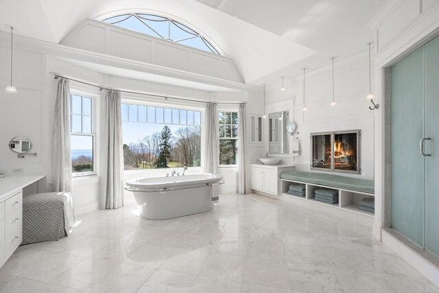 full bathroom featuring a freestanding bath, vaulted ceiling, a glass covered fireplace, marble finish floor, and vanity