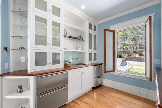 bar featuring a sink, fridge, light wood-type flooring, baseboards, and crown molding