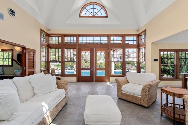 living room featuring plenty of natural light, french doors, stone tile flooring, and high vaulted ceiling