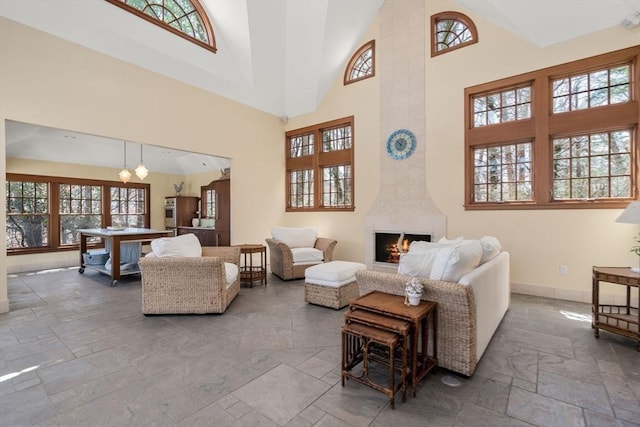 living area featuring stone tile floors, a fireplace, baseboards, and high vaulted ceiling
